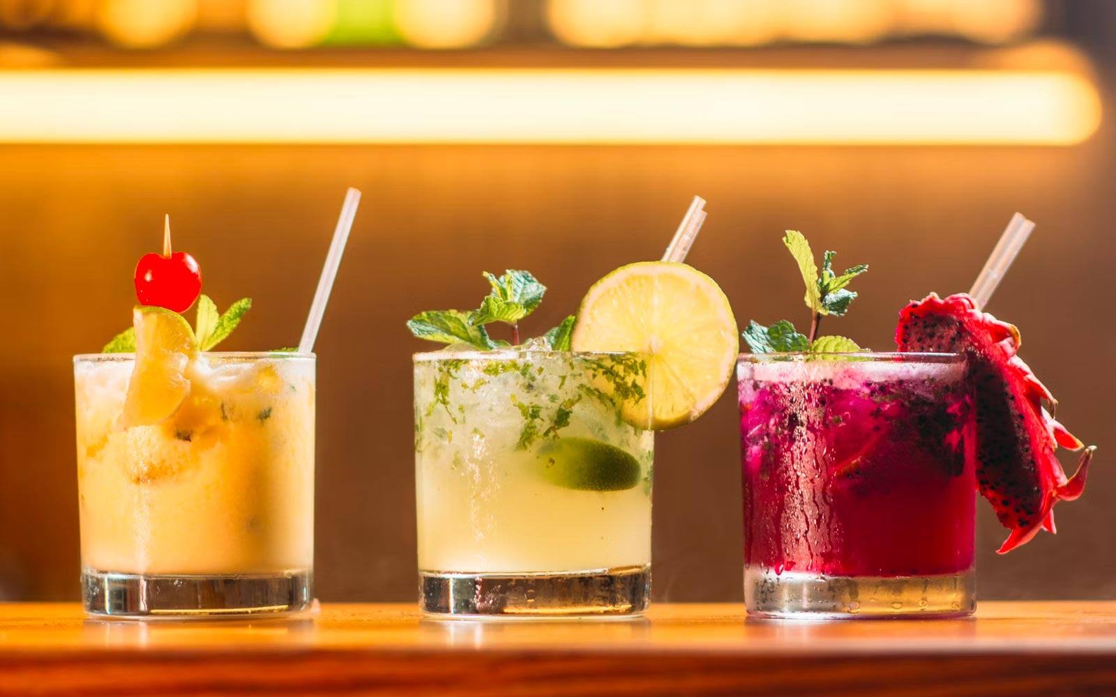 Three garnished cocktails lined up on a bar